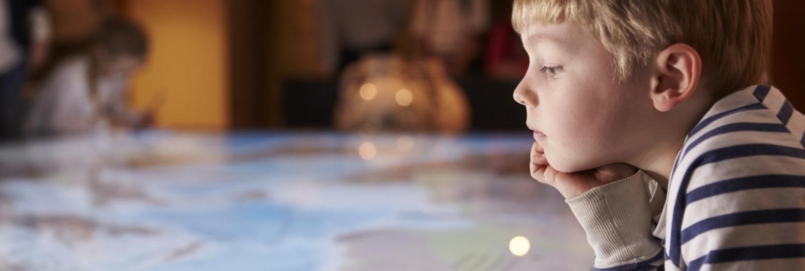 Dreng på 4-5 år med stribet trøje kigger ned på på et kort